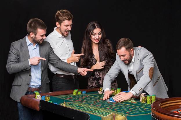 group of young people behind roulette table on black background. the young man rejoices victory